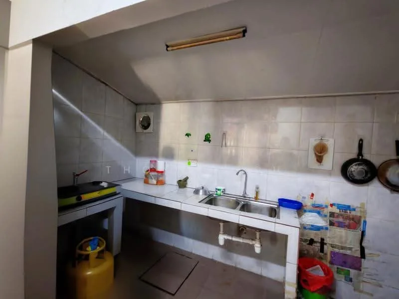 Kitchen features: white tiled walls, grey tiled flooring, single-bowl stainless-steel sink, chrome faucet, kitchen countertop with storage underneath, gas stove with yellow gas cylinder, hanging pots and pans, wall-mounted shelves, various containers and utensils.