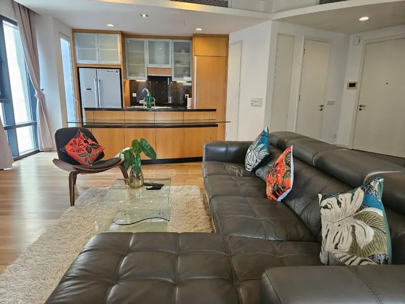 Living features: L-shape sectional sofa in dark brown leather, decorative throw pillows with floral pattern, glass coffee table, area rug with soft texture, wooden flooring, floor-to-ceiling windows, kitchenette with wooden cabinetry, stainless-steel fridge, black countertop, recessed downlights, wall-mounted TV, decorative plant; style: modern; view: city.