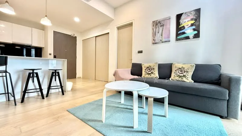 Living features: grey fabric sofa, 2 white coffee tables, light blue area rug, wall-mounted artwork with abstract designs, wooden flooring, recessed ceiling lights, open-plan layout to kitchen, floor-to-ceiling windows, neutral painted walls; style: modern. Kitchen features: white cabinetry, black countertop, stools at kitchen island, refrigerator, built-in oven, ceramic tile backsplash, pendant lighting over island; style: modern.