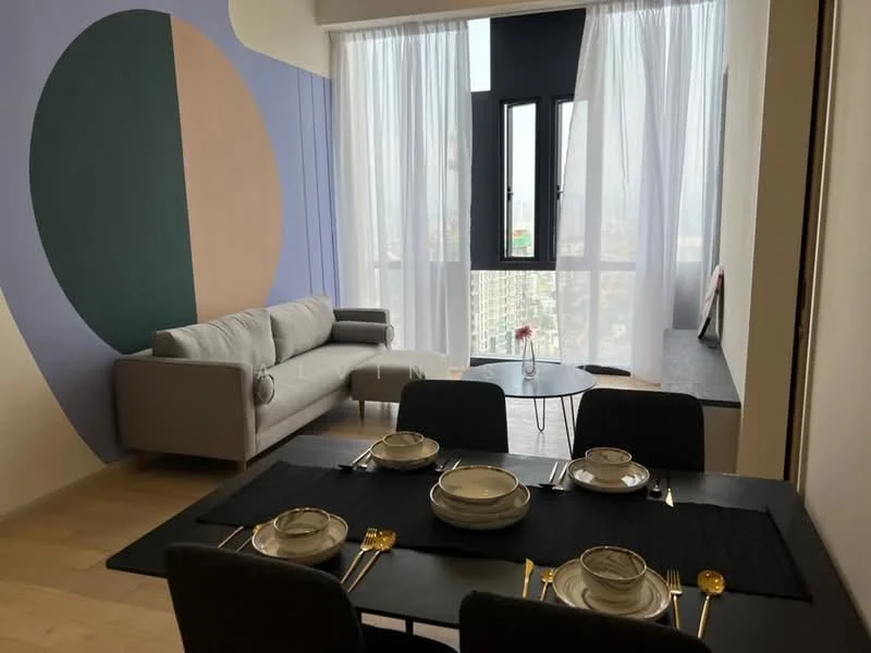 Living features: grey fabric sofa, round coffee table, floor-to-ceiling windows, sheer curtains, decorative wall with geometric patterns, light wood flooring, wall-mounted shelf, city view; style: modern; view: city. Dining features: black dining table, 4 dining plates, gold cutlery, black table runner, decorative flower vase; style: modern.