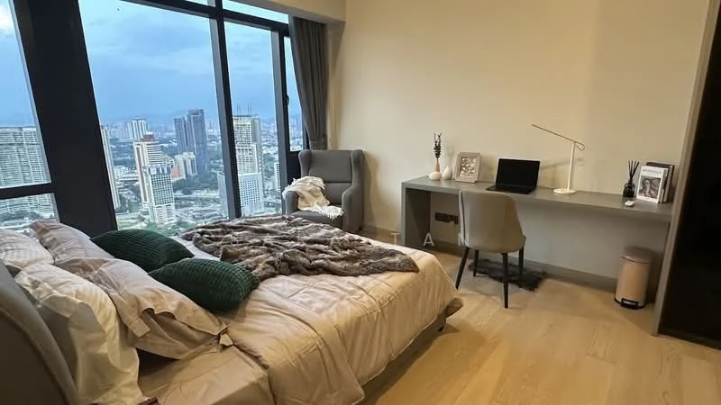 Bedroom features: king-size bed with beige bedding, green decorative pillows, wooden flooring, floor-to-ceiling windows with city view, grey upholstered armchair, desk with laptop, desk lamp, framed photo on desk, decorative plant on desk, light-colored walls, curtains, throw blanket on bed; style: modern; view: city.