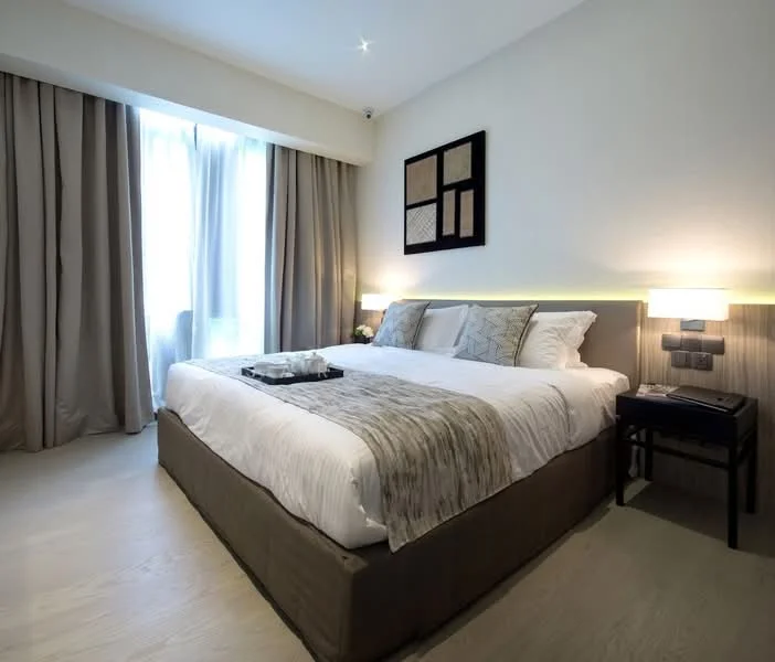 Bedroom features: king-size bed, upholstered headboard, white bedding with decorative throw, bedside tables, wall-mounted lamps, floor-to-ceiling windows, sheer curtains, wooden flooring, decorative wall art, recessed ceiling lights; style: modern.