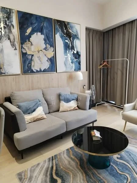 Living features: 3-seater fabric sofa in grey, decorative cushions, round coffee table with black glass top, area rug with abstract pattern, framed artwork with floral and abstract designs, wood panel accent wall, floor-to-ceiling curtains, clothing rack, standing fan; style: modern.