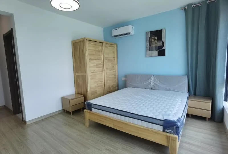 Bedroom features: queen-size bed, upholstered headboard, wooden bed frame, built-in wardrobe with sliding doors, two bedside tables, laminate flooring, blue accent wall, white painted walls, wall-mounted air conditioning unit, curtains in grey, ceiling light fixture; style: modern.