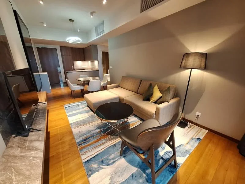 Living features: 3-seater fabric sofa in beige, coffee table with round glass top, area rug with abstract pattern, wall-mounted TV, TV console, floor lamp with fabric shade, wooden flooring, recessed downlights, open-plan layout to dining area, decorative cushions, wall with neutral paint, large window with natural light; style: modern.
