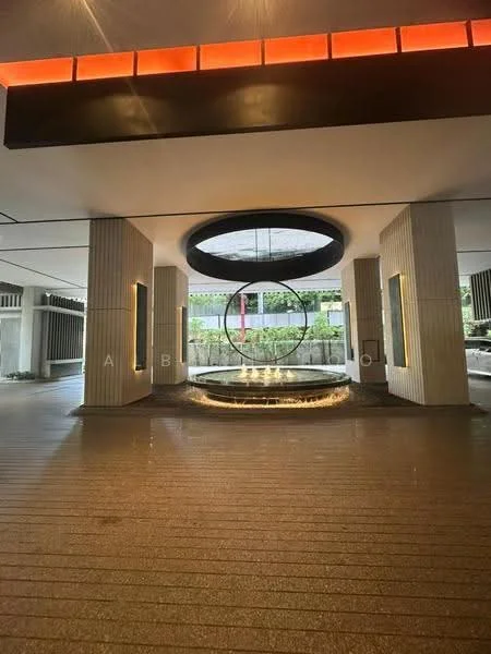 Exterior type: lobby; features: modern circular water feature, textured stone flooring, vertical concrete columns, large circular skylight, greenery visible in background, ambient lighting, recessed wall lighting, decorative wall panels, open layout, contemporary design elements; style: modern.