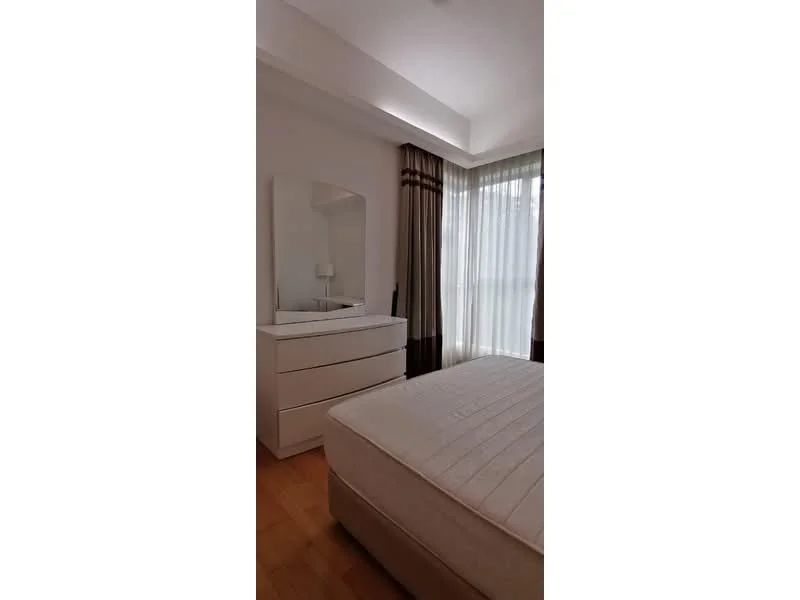 Bedroom features: queen-size bed, white bedding, white dresser with drawers, full-length mirror, floor-to-ceiling windows, sheer curtains, wooden flooring, decorative wall with light color, table lamp on dresser; style: modern.