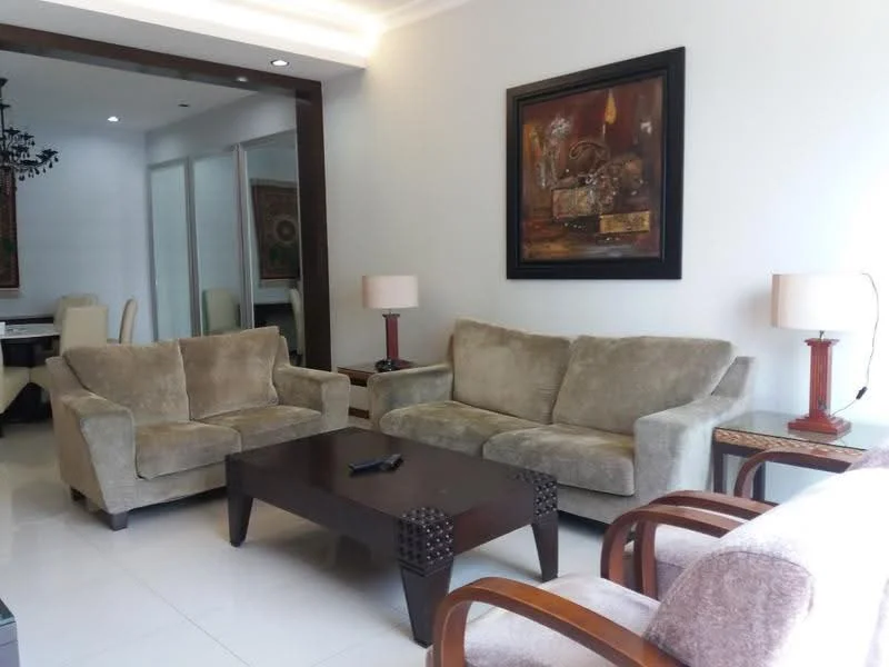 Living features: 2-seater fabric sofa in beige, 3-seater fabric sofa in beige, wooden coffee table with decorative legs, table lamp with fabric shade, wall-mounted artwork with abstract design, recessed ceiling lights, white painted walls, glossy tile flooring, decorative wall paneling, open layout to dining area; style: contemporary.