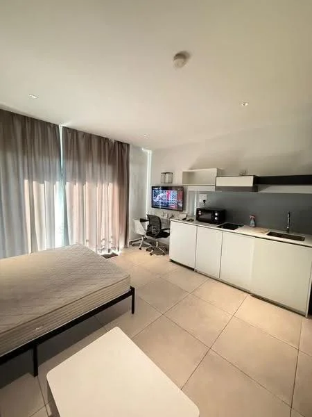 Room features: queen-size bed frame without mattress, floor-to-ceiling windows with sheer curtains, light grey tiled flooring, white painted walls, white cabinetry, kitchenette with sink, black countertop, built-in microwave, small dining table, office chair, computer monitor on desk, refrigerator, task lighting, open shelving; style: modern.