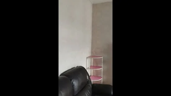 Room features: black leather sofa, light-colored painted walls, textured wallpaper, white shelving unit with pink shelves.