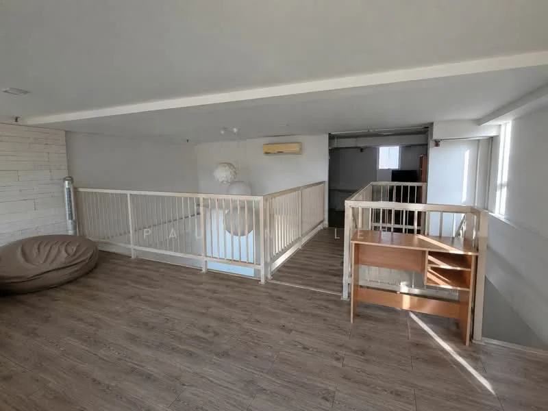 Room features: wooden flooring, white walls, railing with wooden balustrade, ceiling-mounted air conditioning unit, large windows providing natural light, open space layout, bean bag chair, wooden side table; style: modern.