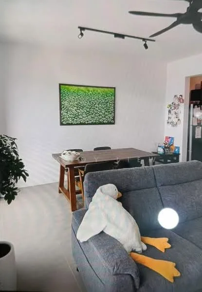 Living features: grey fabric sofa, decorative plush duck, wooden dining table, black dining chairs, green artwork on wall, recessed lighting, ceiling fan, potted plant, light-colored tile flooring, open layout, wall-mounted storage, kitchen area visible; style: modern.