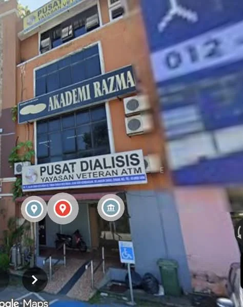 Exterior features: multi-storey building, signage for Akademi Razma, signage for Pusat Dialisis, ATM visible, entrance with glass doors, parking area visible, bicycle parking, green waste bin; style: modern.
