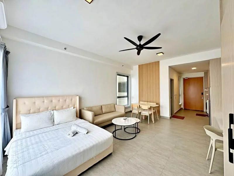 Living features: queen-size bed with upholstered headboard, sofa in beige fabric, round coffee table with black metal frame, wall-mounted TV, ceiling fan with light, light grey tiled flooring, white painted walls, large window with sheer curtains, wood panel accent wall, entrance door with security lock, open layout to hallway; style: modern.