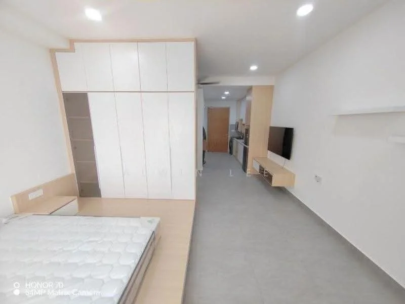 Room features: light grey tiled flooring, white painted walls, built-in wardrobe with white doors, wooden bed frame, mattress on bed, wall-mounted TV, floating shelf, ceiling lights, open layout, kitchen area visible in background, refrigerator visible in background; style: modern.