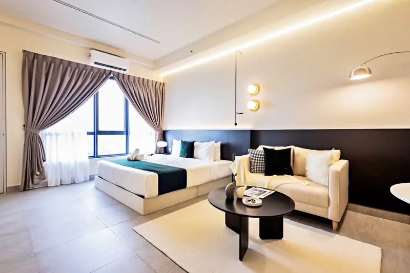 Bedroom features: queen-size bed with white bedding, upholstered headboard, 2 bedside lamps, sofa in cream fabric, black coffee table, area rug in neutral color, floor-to-ceiling window with sheer curtains, wall-mounted light fixture, air conditioning unit, decorative cushions, accent wall in black, light wood flooring, recessed LED lighting; style: modern; view: city.