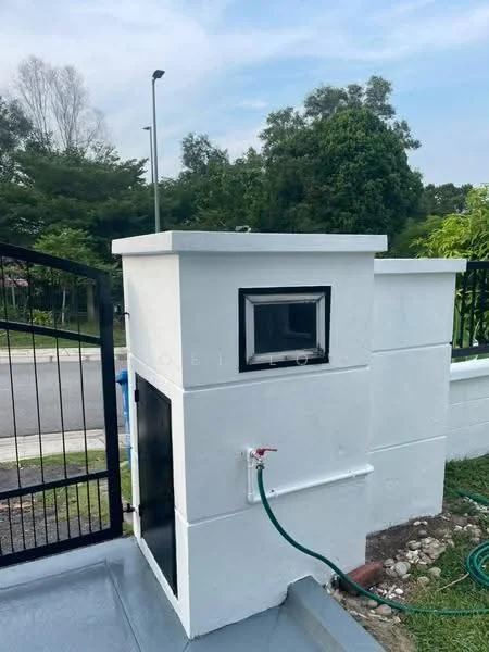 Exterior type: main entrance gate; features: white painted facade, security intercom panel, metal gate, landscaped greenery in background, driveway with interlocking pavers, water tap with hose connection; style: modern.