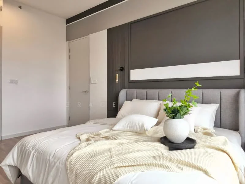Bedroom features: king-size bed with grey upholstered headboard, white bedding with decorative pillows, light-colored throw blanket, decorative plant in a ceramic pot, wall-mounted reading light, neutral wall color, accent wall with vertical paneling, floor-to-ceiling window, light wood flooring, built-in wardrobe, minimalist decor; style: modern.