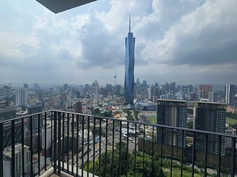 Exterior type: high-rise condominium; features: city skyline view, balcony with railing, surrounding urban landscape, visible high-rise buildings, Petronas Twin Towers in view, Merdeka 118 in view, cloudy sky, greenery at lower levels; style: modern.