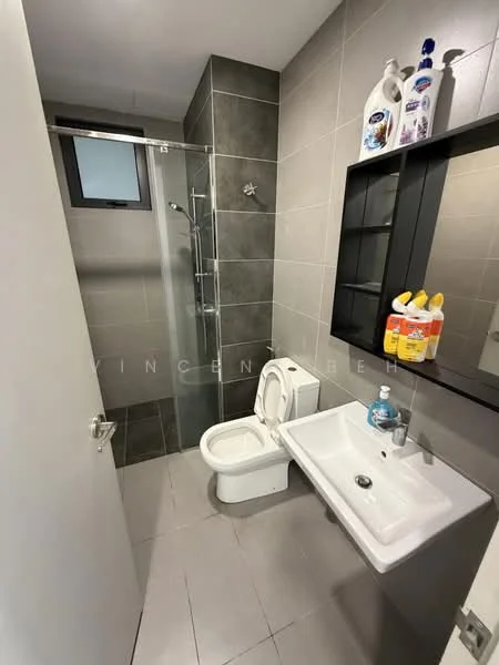 Bathroom features: grey tiled walls, grey tiled flooring, glass shower enclosure, rain shower head, handheld shower, single-sink vanity with white cabinet, chrome basin mixer, one-piece toilet, mirror above sink, shelf with cleaning products; style: modern.
