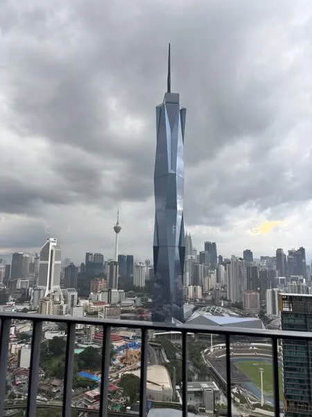 Exterior type: high-rise condominium; features: glass curtain wall, modern architectural design, surrounded by city skyline, view of Merdeka 118, view of KL Tower, urban landscape, cloudy sky, balcony railing; style: modern.