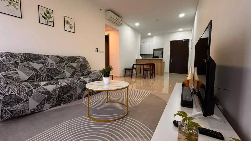 Living features: 3-seater fabric sofa with geometric pattern, round coffee table with gold metal base, area rug with abstract pattern, wall-mounted TV, TV console with storage, decorative plants, framed artwork on walls, recessed downlights, air conditioning unit; style: modern. Kitchen features: open kitchen layout, white cabinetry, stainless-steel appliances, kitchen island with seating, light-colored countertops, tile backsplash; style: modern.