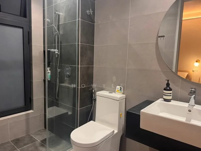 Bathroom features: walk-in shower with glass enclosure, chrome handheld shower, black wall-mounted faucet, white ceramic sink, black countertop, one-piece toilet, grey tile flooring, grey wall tiles, round mirror, bathroom accessories, shelf with toiletries; style: modern.