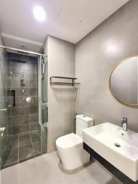 Bathroom features: grey ceramic tile flooring, grey tiled walls, walk-in shower with glass enclosure, rain shower head, handheld shower, chrome basin mixer faucet, white wall-mounted sink, one-piece toilet, framed round mirror, towel rack, recessed lighting; style: modern.