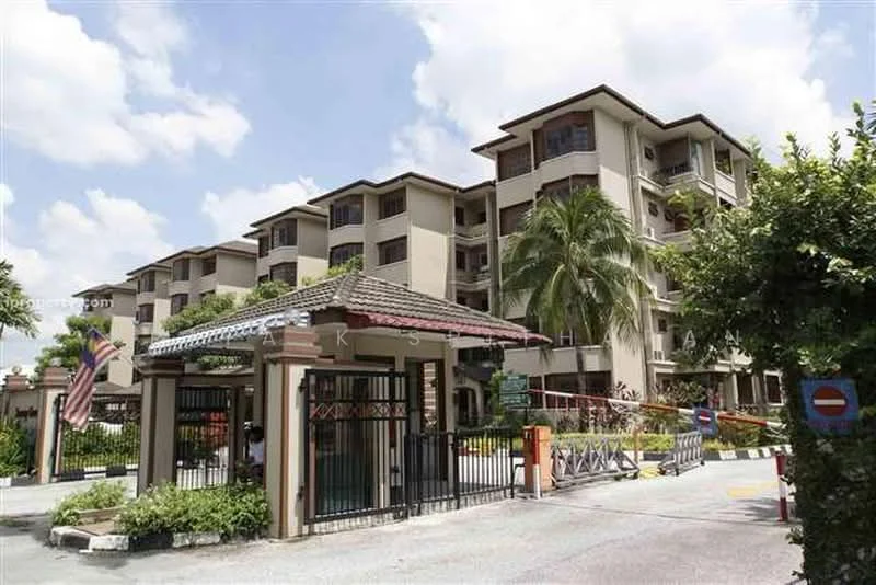 Exterior type: low-rise apartment block; features: gated entrance, manicured landscaping, palm trees, multiple storeys, balconies on upper floors, security guard house, driveway with interlocking pavers, flagpole with Malaysian flag, surrounded by greenery, decorative fencing; style: modern.