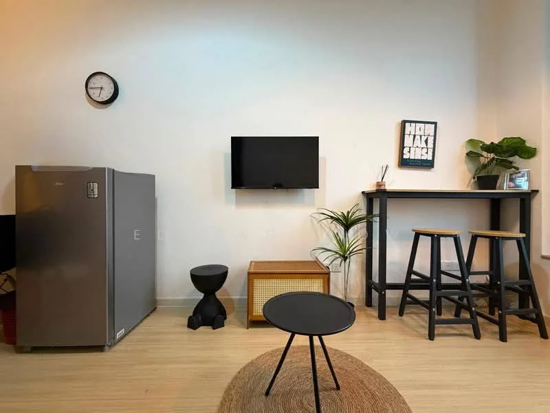 Living features: grey fridge, wall-mounted TV, wooden TV console, black round coffee table, black stool, wooden bar table, two wooden bar stools, wall clock, decorative plant, framed artwork with text; style: modern.