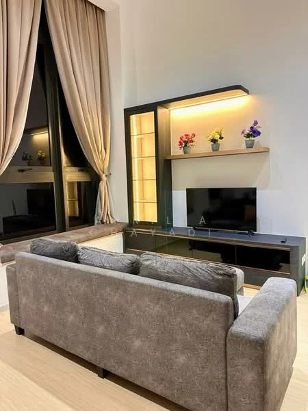 Living features: grey fabric 3-seater sofa, black TV console, wall-mounted TV, built-in shelving unit with lighting, decorative flowers on shelves, floor-to-ceiling windows, sheer curtains, light wood flooring; style: modern.