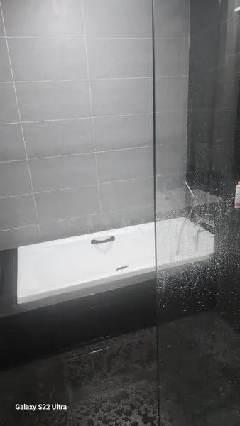 Bathroom features: built-in bathtub, glass shower enclosure, black tile flooring, grey wall tiles, chrome faucet, wall-mounted showerhead, black vanity unit, mirror above vanity; style: modern.