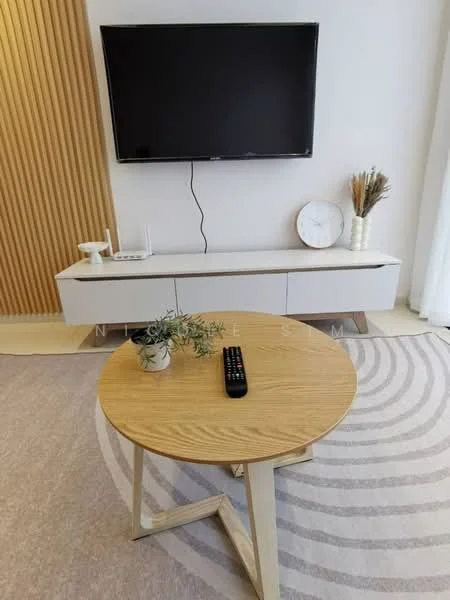 Living features: wall-mounted flat-screen TV, white TV console with drawers, round wooden coffee table, area rug with circular pattern, decorative wall with wooden slats, decorative clock, dried flower arrangement, remote control on coffee table; style: modern.