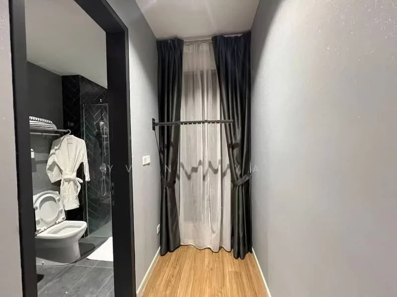 Room features: grey painted walls, wooden flooring, floor-to-ceiling windows, sheer curtains, blackout curtains, towel rack, bathrobe hanging, doorway leading to bathroom, visible toilet, glass shower enclosure, black tile flooring, white toilet; style: modern.