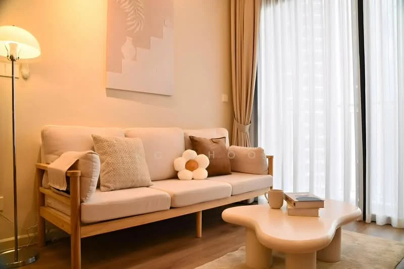 Living features: light beige fabric sofa, wooden frame sofa, decorative cushions in various colors, round coffee table with soft edges, floor lamp with white shade, light wood flooring, curtains in light beige, wall art with abstract design, large glass windows, natural light from windows; style: modern.