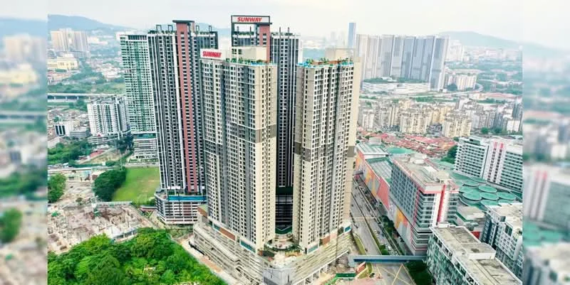 Exterior type: high-rise condominium; features: glass curtain wall, exposed concrete facade, recessed balconies, multiple storeys, surrounded by mature greenery, urban context with city skyline in background; style: modern.