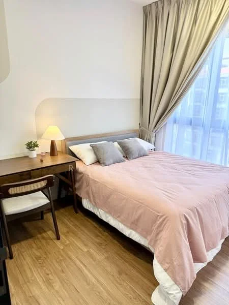 Bedroom features: queen-size bed with pink bedding, two grey decorative pillows, wooden bedside table, table lamp on bedside table, study desk with chair, curtains in light beige, floor-to-ceiling windows, wooden flooring, houseplant in ceramic pot; style: modern.