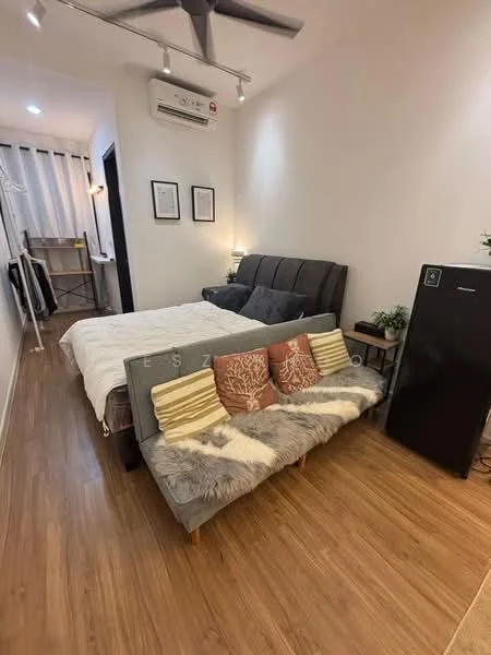 Room features: queen-size bed with upholstered headboard, 2-seater fabric sofa in grey, wooden flooring, wall-mounted split AC, recessed downlights, decorative cushions on sofa, framed artwork on walls, small side table, black fridge, shelves with decorative items, light-colored bedding; style: modern.