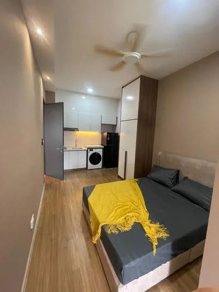 Bedroom features: queen-size bed with grey bedding, yellow throw blanket, wooden flooring, light brown painted walls, ceiling fan, built-in wardrobe with sliding doors, kitchenette with white cabinets, black refrigerator, front-load washing machine, countertop with sink, stainless-steel faucet, recessed lighting; style: modern.