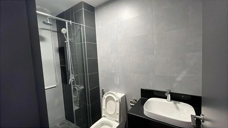 Bathroom features: grey tile flooring, grey wall tiles, glass shower enclosure, rain shower head, handheld shower, single-sink vanity with black countertop, white basin, one-piece toilet, chrome faucet, mirror above sink, towel rack; style: modern.