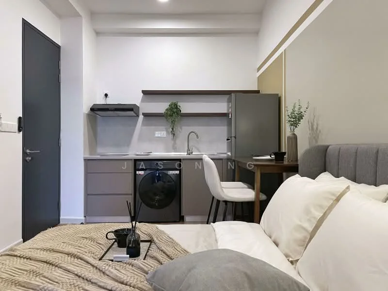 Room features: grey upholstered headboard, queen-size bed, white bedding, beige throw blanket, small black coffee table, black decorative items, white wall with light grey accent, kitchenette with grey cabinets, stainless-steel sink, chrome pull-down faucet, built-in stove, refrigerator, front-load washing machine, bar stool, wall-mounted shelving; style: modern.