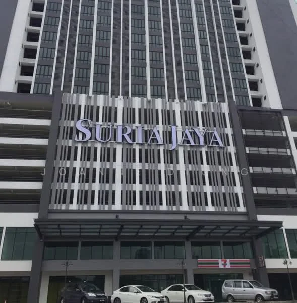 Exterior type: mid-rise condominium; features: glass curtain wall, white painted facade, projecting balconies, feature lighting at night, 7-Eleven store at ground level, multiple parking spaces visible, signage with 'SURIA JAYA', modern architectural design; style: modern.