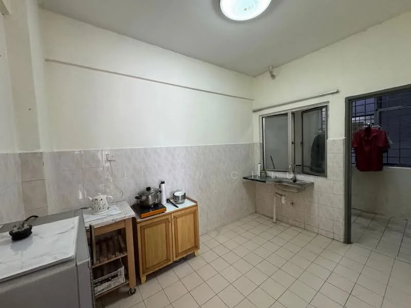 Kitchen features: white painted walls, cream tiled backsplash, light grey floor tiles, single-bowl stainless-steel sink, chrome pull-down faucet, wooden cabinetry, countertop with space for appliances, window with metal grille, exposed plumbing, kitchen appliances including a stove, open shelving, laundry area with hanging clothes.