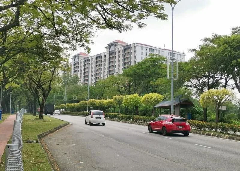 Exterior type: mid-rise condominium; features: 6-storey building, glass curtain wall, surrounded by mature greenery, manicured lawn, trees lining the road, paved walkway, street lighting, parking spaces visible, adjacent to main road; style: modern.