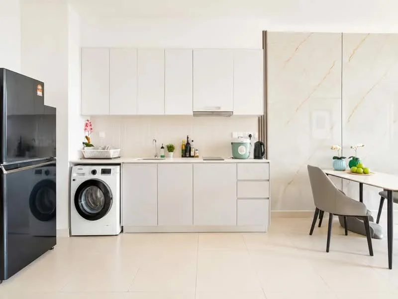 Kitchen features: white cabinetry, black refrigerator, front-load washing machine, stainless-steel sink, chrome pull-down faucet, white countertop, tile backsplash, built-in oven, microwave, kitchen island, dining table, upholstered dining chairs, decorative plants; style: modern.
