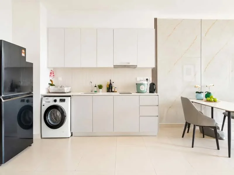 Kitchen features: white cabinetry, black refrigerator, front-load washing machine, stainless-steel sink, chrome pull-down faucet, white countertop, tile backsplash, built-in oven, kitchen island, dining table with chairs, decorative plants; style: modern.
