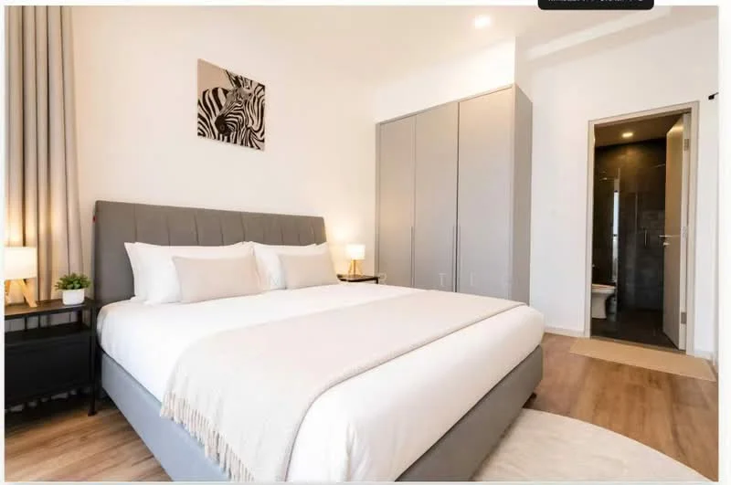 Bedroom features: king-size bed with grey upholstered headboard, white bedding with decorative throw, two bedside lamps with white shades, grey built-in wardrobe with sliding doors, wooden flooring, framed artwork with zebra print on wall, curtains in light grey, neutral wall color, doorway leading to bathroom, area rug at the foot of the bed; style: modern.
