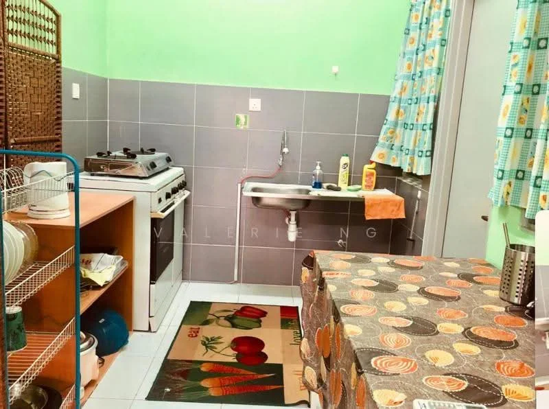 Kitchen features: green painted walls, grey tiled backsplash, white ceramic tile flooring, stainless-steel sink, chrome faucet, 4-burner gas hob, freestanding oven, wooden countertop, kitchen island with patterned tablecloth, curtains with colorful pattern, open shelving with dishes, rug with fruit design.
