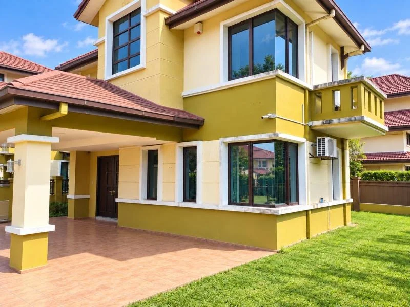 Exterior type: detached bungalow; features: double-storey, cream and yellow painted facade, pitched tile roof, projecting roof eaves, recessed balcony, corner windows, large glazed windows, covered car porch with awning, tiled driveway and porch flooring, manicured lawn, fronts a quiet residential street, surrounded by neighboring houses; style: contemporary.