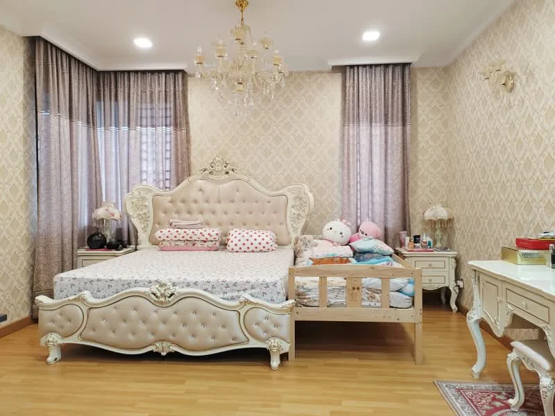 Bedroom features: king-size bed with upholstered headboard, bedside tables with lamps, wooden flooring, chandelier light fixture, curtains with sheer and patterned fabric, decorative wall with floral pattern, stuffed toys on bed, small wooden bed frame for child, dressing table with mirror; style: luxury.
